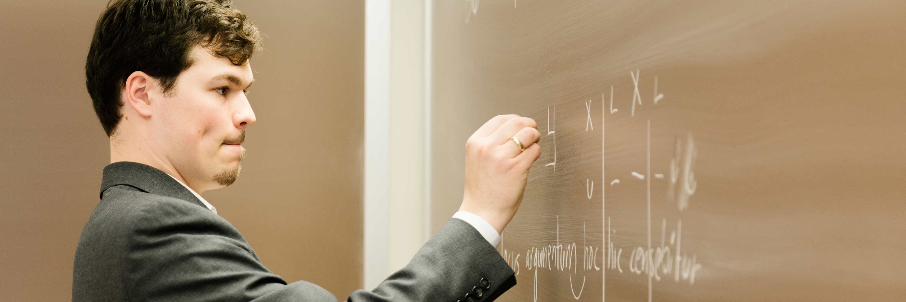 A student writing Latin on a chalkboard.
